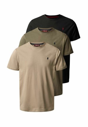 Mężczyzna stoi i się uśmiecha, ubrany w beżowy t-shirt, ciemne dżinsy i brązowe sznurowane buty na jasnym, jednolitym tle.