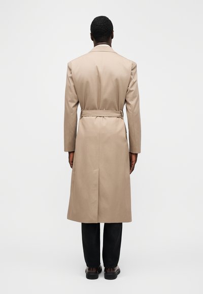 Gabardina beige con cinturón en la cintura, mangas largas y abertura en la parte posterior. La tela parece suave con una silueta limpia y entallada.