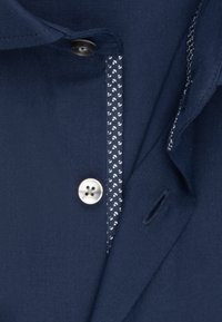 Close-up of a navy blue blazer with a white four-hole button and a patterned trim with small white shapes along the inner edge.