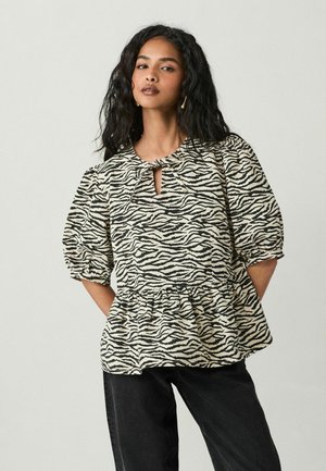 Haut à imprimé zèbre noir et crème avec un décolleté en trou de serrure, des manches bouffantes et un ourlet à volants, fabriqué en tissu texturé. Associé à un pantalon noir.