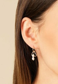 Goldene Creolen schmücken einen herzförmigen Anhänger, von dem zwei weiße Perlen herabhängen. Das Design ist filigran und verstärkt die gesamte Eleganz.