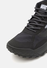 Svarta Vans-sneakers med en strukturerad ovandel, förstärkt gummisula och kontrasterande platta svarta snören med mönstrad detalj.