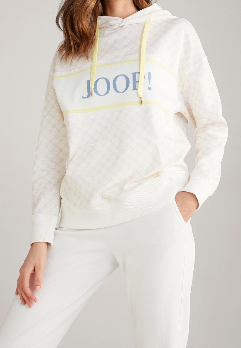 White hoodie with subtle patterned texture, yellow drawstrings, and blue "JOOP!" logo across the chest, paired with white pants.