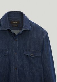 Donkerblauw denimshirt met een puntige kraag, voorzien van twee borstzakken, knoopsluitingen en een gestructureerde stof.