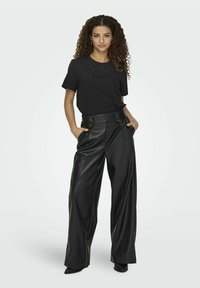 Camiseta de algodón negra con mangas cortas y detalles decorativos, combinada con pantalones de pierna ancha de imitación cuero negros de cintura alta.