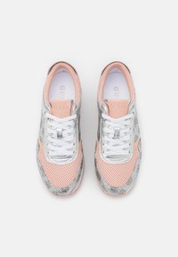 Een paar roze en zilveren lage sneakers met witte veters, mesh stof en "Guess" branding op de tong en de binnenzool.