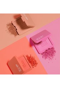 Trois blushs compacts avec des textures lisses. Les couleurs incluent un pêche doux, un corail vibrant et un rose pastel, chacun avec un étui assorti.