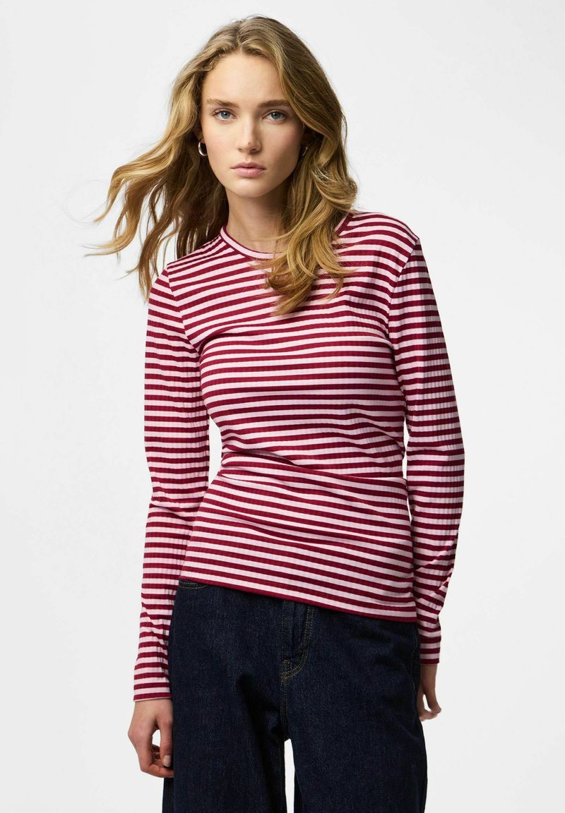 Rot-weiß gestreiftes Langarmshirt mit rundem Ausschnitt aus geripptem Stoff. Die Ärmel sind enganliegend und an den Bündchen leicht ausgestellt.