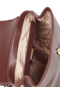 Brun läderhandväska med ett guldmagnetstängning. Inuti finns en beige foder och en ficka med blixtlås med präglat mönster.