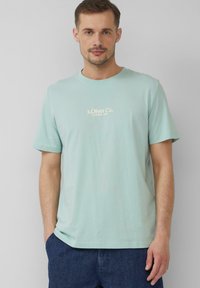 Jasnozielona bawełniana koszulka z okrągłym dekoltem. Posiada mały, kremowy tekst logo na piersi. Krótkie rękawy i luźny krój.