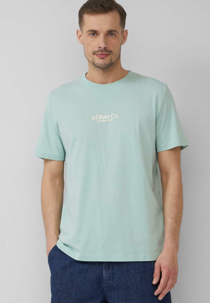 Jasnozielona bawełniana koszulka z okrągłym dekoltem. Posiada mały, kremowy tekst logo na piersi. Krótkie rękawy i luźny krój.