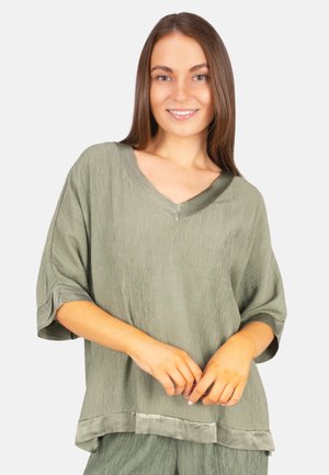 Olivgrüne, locker sitzende Bluse mit V-Ausschnitt, strukturiertem Stoff und kurzen, umgeschlagenen Ärmeln. Mit einem Satinbesatz am Saum.
