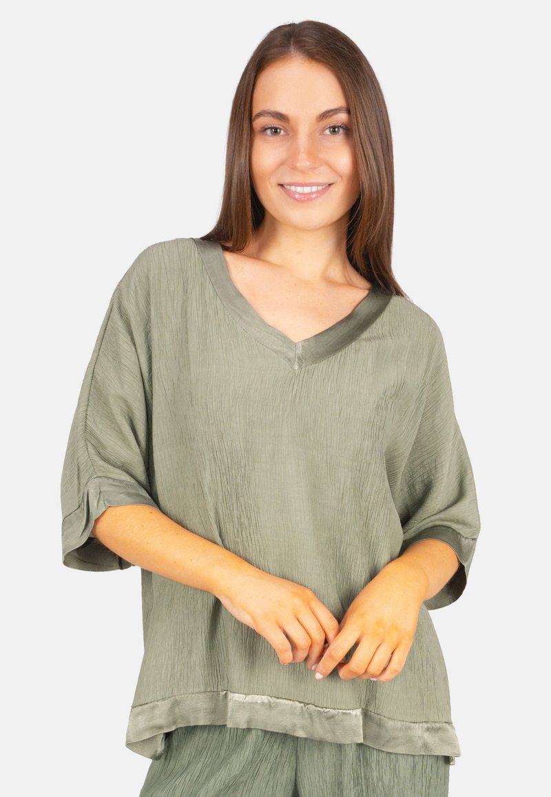 Olivgrüne, locker sitzende Bluse mit V-Ausschnitt, strukturiertem Stoff und kurzen, umgeschlagenen Ärmeln. Mit einem Satinbesatz am Saum.