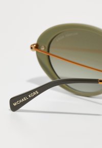 Michael Kors solbriller med olivengrønne linser, trådramme med guldsmykker og en sort templet med mærkenavnet i guldtekst.