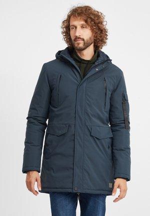 Parka aislante de color azul marino con capucha, cierre frontal con cremallera, dos bolsillos delanteros y un bolsillo en la manga con cremallera y detalle de logo.