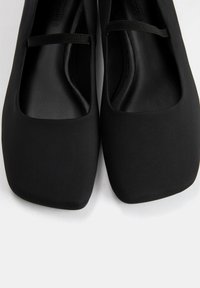Schwarze Ballettflats aus glattem Material mit einem quadratischen Zehen-Design und einem dekorativen Riemen oben. Das Innere ist strukturiert.