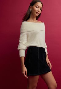 Off-white fluffy sweater with off-the-shoulder design, paired with a black denim mini skirt featuring visible stitching details.