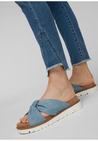 Blå knutna slidesandaler med en texturerad mockaovandel, brun fotbädd och vit gummisula, kombinerat med jeans med fransad nederkant.