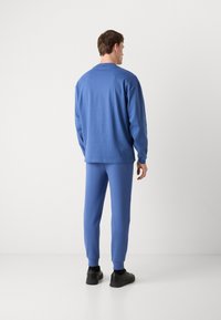 Blue cotton sweatshirt and matching joggers, both with a relaxed fit, ribbed cuffs, and a smooth texture. Black sneakers complete the outfit.