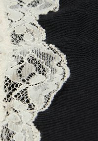 Czarna tkanina z misternym, off-white koronkowym wykończeniem o wzorze kwiatowym, ukazująca delikatne detale i fakturę wzdłuż krawędzi.