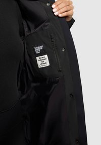 Black insulated coat featuring a smooth inner lining, secure zipper pocket, and label with brand and care instructions sewn inside.