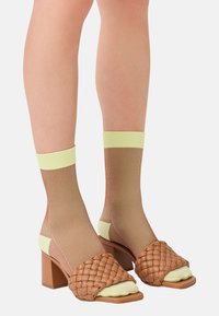 Braune geflochtene Sandalen mit Absätzen und einem gelben Band, kombiniert mit gerippten Kniestrümpfen in hellgrünen und braunen Farbtönen. Blockabsatzdesign.