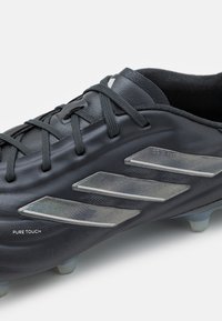 Scarpa da calcio nera con tomaia in pelle liscia, caratterizzata da un design a tre strisce metalliche argento, dettagli testurizzati e lacci grigi.