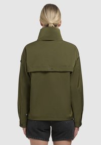 Veste légère olive, avec un col haut et un détail de rabat au dos, dotée de poignets boutonnés et d'un logo subtil au dos.