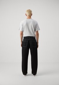 Graues T-Shirt mit kurzen Ärmeln kombiniert mit hochg 증가mmten schwarzen Jeans im weiten Schnitt. Sichtbare hintere Taschen und weiße Nahtdetails an den Jeans.