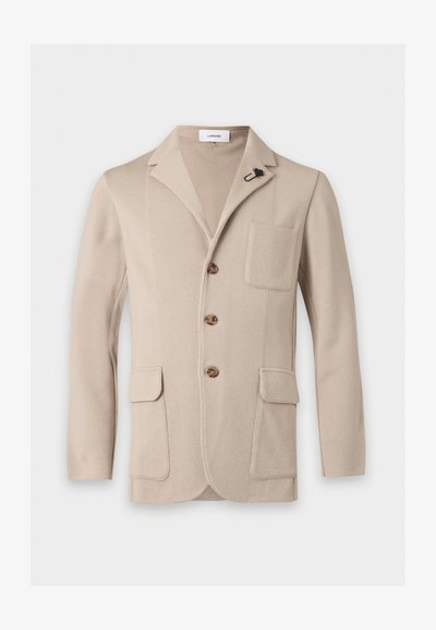 Blazer en maille beige avec revers crantés, trois boutons marron, une poche poitrine, deux poches avant à rabat et une épingle florale noire sur le revers.