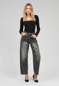 Haut noir à manches longues associé à un jean gris taille haute à jambes larges présentant une finition texturée et des accents cloutés, complété par des talons noirs.