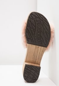 Dřevěná podešev sandálů s černou gumovou podrážkou, která má měkké růžové kožíškové akcenty. Jasný otisk loga na gumě. Design zaměřený na pohodlí.