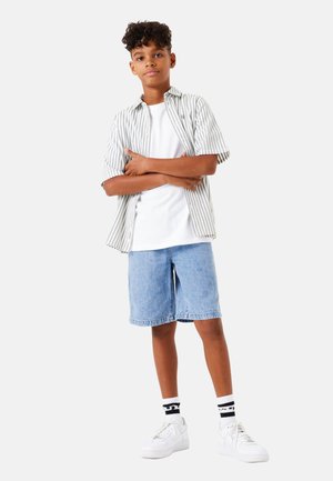 Chemise à rayures grise et blanche, t-shirt blanc, shorts en denim bleu, baskets blanches et chaussettes rayées noir et blanc.
