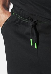 Black athletic shorts with a drawstring featuring green accents. The fabric appears smooth, with contrasting green stitching near the waistband.