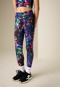 Färgglada, stretchiga leggings med ett stänkigt mönster i grönt, blått, rosa och lila, kombinerade med svarta sneakers och vita strumpor.