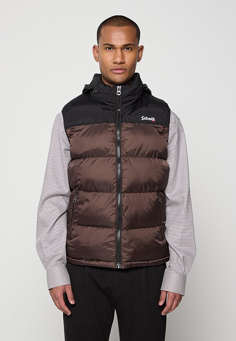 Gilet rembourré marron et noir avec une fermeture éclair à l'avant, capuche ajustable et détails de logo. Porté par-dessus une chemise à carreaux grise. Texture lisse.
