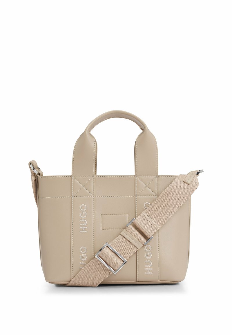 Beige handbag made of smooth synthetic material; features quilted design, dual top handles, adjustable strap, and logo accents.