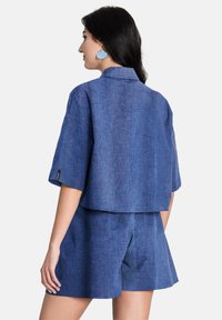 Avskuren blå skjorta i strukturerad tyg med breda ärmar, parat med matchande shorts, vilket visar en avslappnad passform och krage-design.