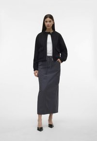 Svart kort jakke med to frontlommer, kombinert med en grå, midtlengde skjørt med sidelomme. Modellen har på seg svarte spisse flate sko.