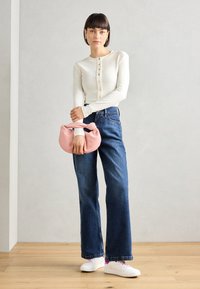 Vit ribbad långärmad topp med knapppdetalj, blå högmidjade vida jeans, rosa knuten handväska, och vita sneakers. Släta texturer.