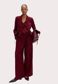 Burgundy suit with ruffled blouse, wide-leg trousers, and pointed shoes featuring decorative accents. Includes a burgundy handbag.