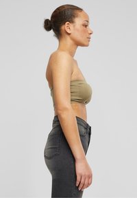 Olivovozelený crop top bez ramienok s hladkým povrchom v kombinácii s vysokými tmavosivými džínsami s jemným prechodom a klasickými vreckami.