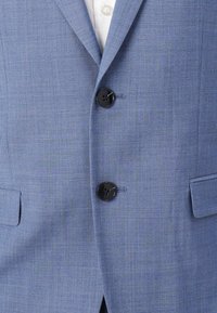 Lichtblauwe blazer van een gestructureerde stof, met twee zwarte knopen en reverskraag, een enkele borstzak en twee zijzakken.