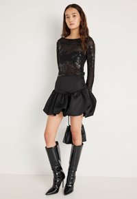 Top de malha preta de manga comprida com detalhes florais em lantejoulas, combinado com uma saia rodada de cetim preta. Botas pretas de salto alto até ao joelho, com acabamento brilhante.