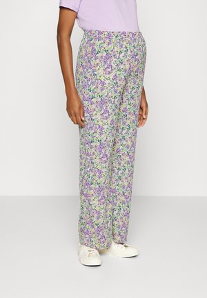 Persona che indossa pantaloni larghi a vita alta con stampa floreale in viola, verde e bianco, con sneakers bianche e una maglietta corta lavanda.