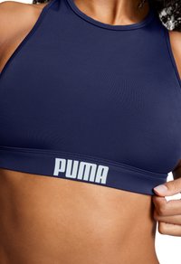 Námorná športová podprsenka vyrobená z hladkej tkaniny, s vysokým golierom a širokým pásom s logom "PUMA" v svetlosivej farbe.