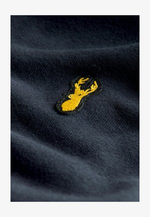 Sötétkék pamutanyag textúrált felülettel, feketével körvonalazott sárga hímzett szarvaslogóval.