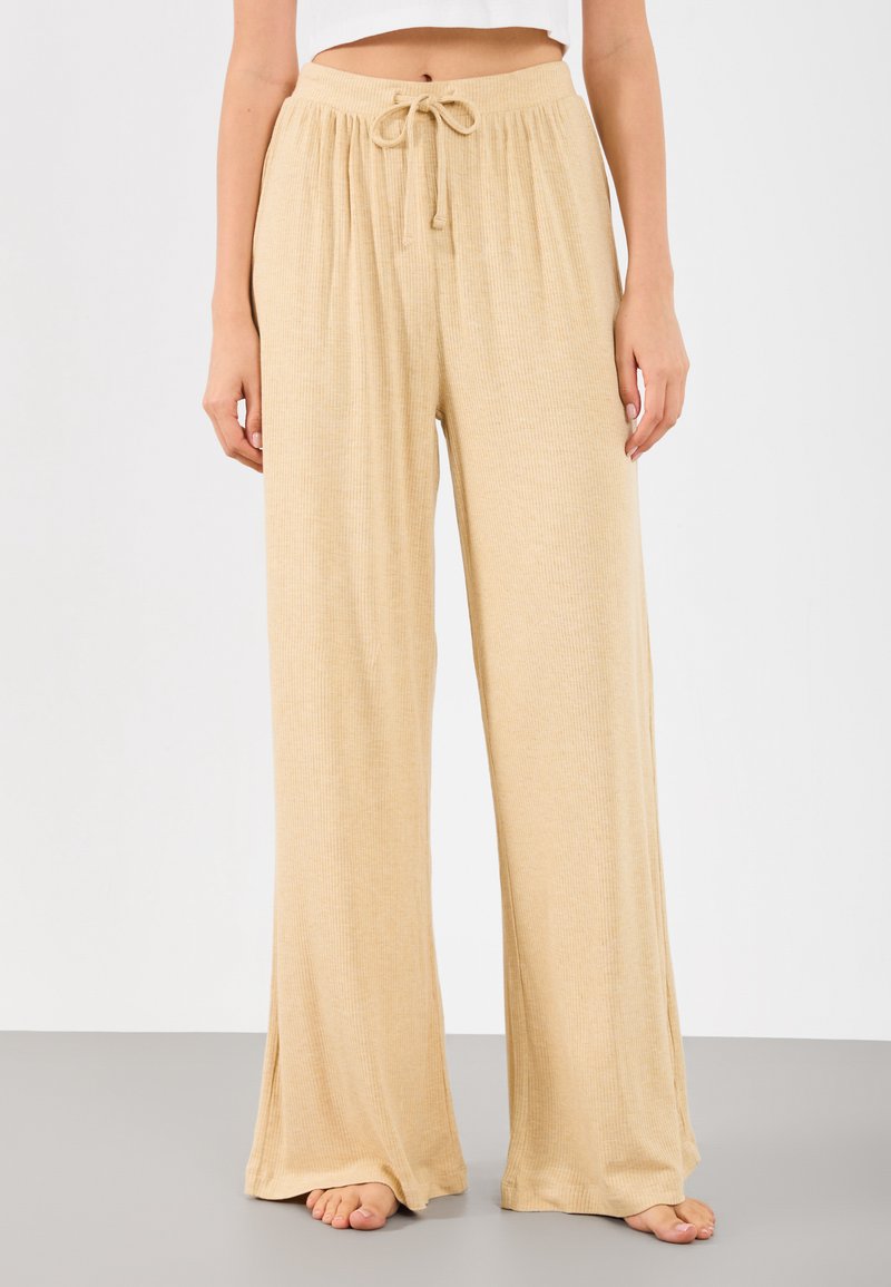 Μπεζ παντελόνι φάρδους με υφή από ραβδωτό ύφασμα. Διαθέτει ελαστική μέση και λεπτομέρεια με κορδόνι στη μπροστινή πλευρά.