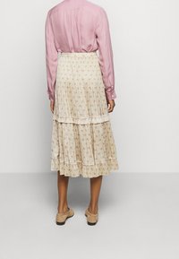 Falda midi floral en tejido ligero, base crema con pequeñas flores rosas, capas acampanadas y sutiles plisados. Combinada con una blusa rosa.