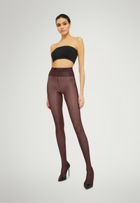 Leggings bordeaux a vita alta opachi con una texture liscia, abbinati a un top nero senza spalline e scarpe con tacco alte nere.